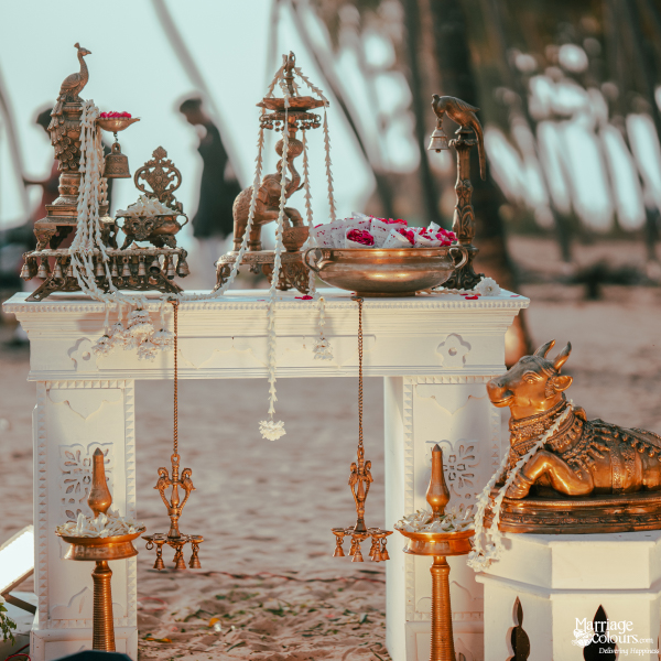 Traditional bronze Nandi cow and brass lamps displayed on a carved white pedestal for a beach ceremony.