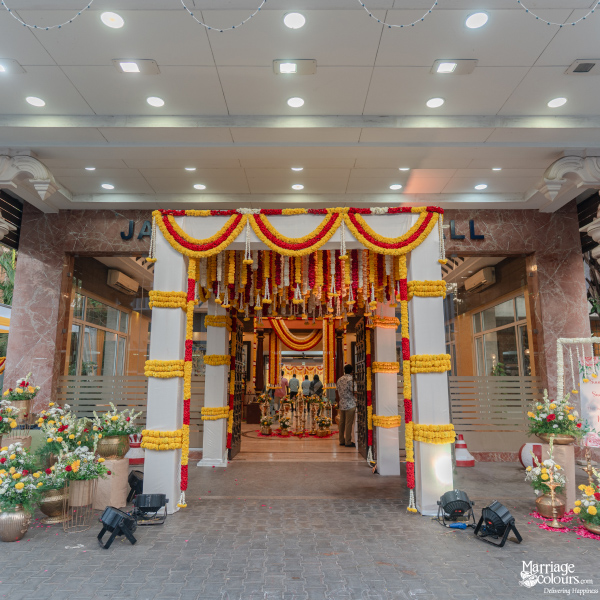 Grand wedding hall entrance decorated with yellow and red flower garlands and white columns.