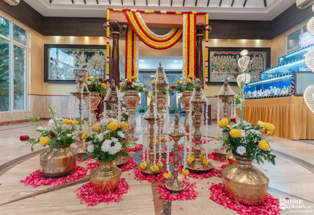 Traditional brass oil lamps and gold pots surrounded by roses and marigolds for a wedding.