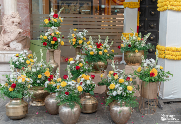Cluster of traditional brass pots and vases holding red, white, and yellow floral arrangements.