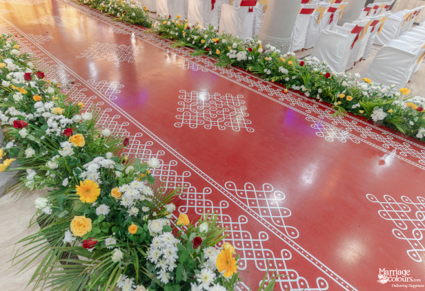 A close-up of a red wedding aisle carpet with white traditional Kolam floor art.