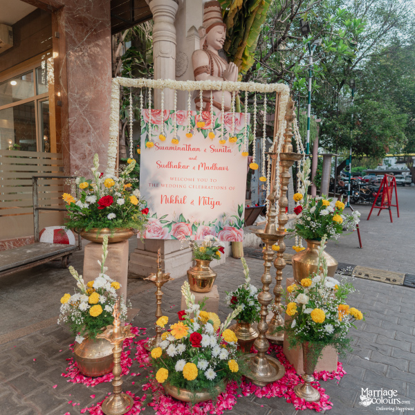 Beautifully decorated wedding welcome sign with a floral border, brass lamps, and rose petals.