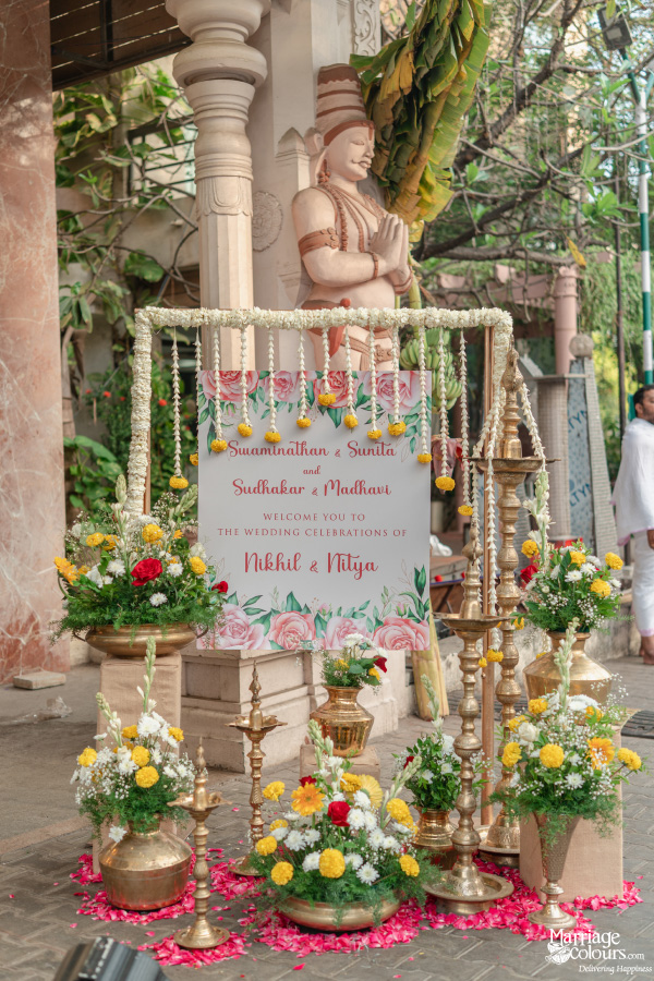 Vibrant Indian wedding entrance decor featuring a floral welcome sign, brass lamps, and flowers.
