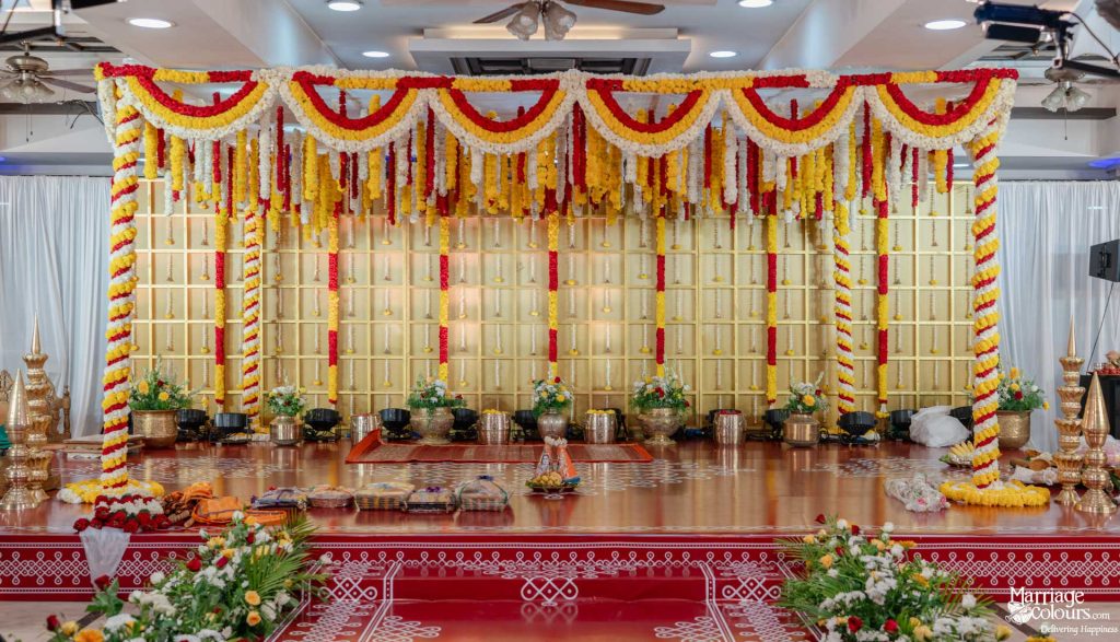 Vibrant Indian ceremonial stage with red and yellow marigold garlands against a gold paneled backdrop.