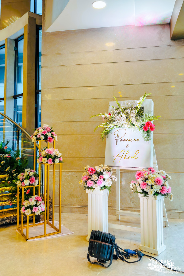 An elegant welcome display for a wedding reception with a sign on an easel and floral arrangements on gold stands and white columns.
