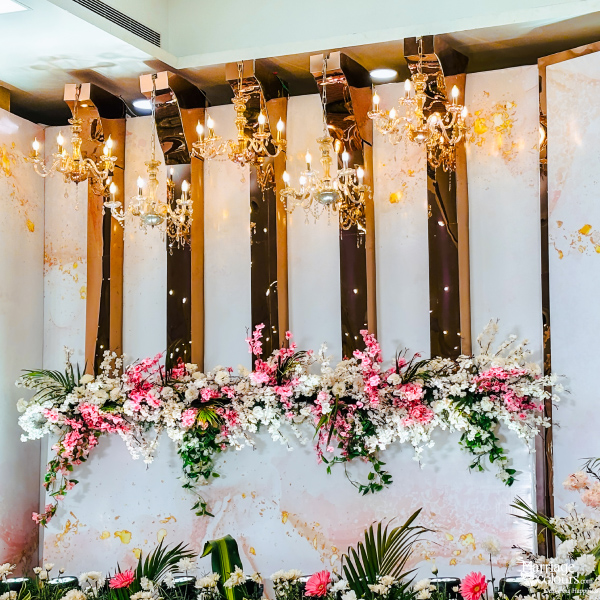 A close-up of a wedding stage backdrop featuring floral garlands, chandeliers, and elegant white and gold panels.