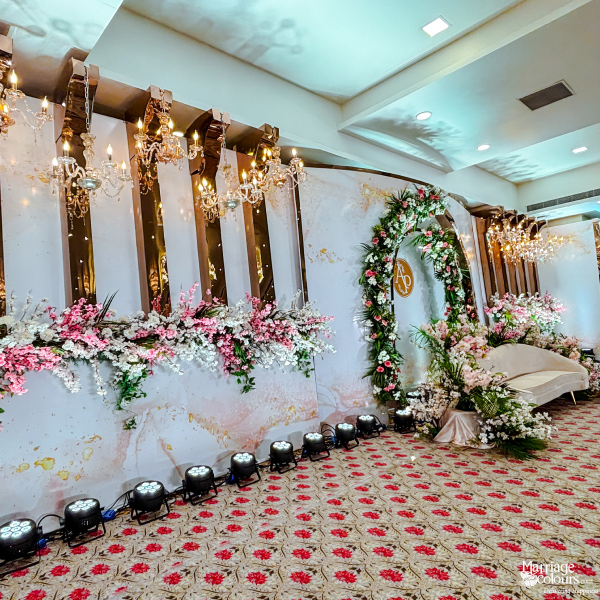 A close-up view of a wedding reception stage with a floral arch, a white sofa, and a marble and white backdrop.