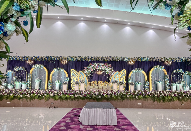 Grand wedding stage with a purple backdrop, blue and white floral decor, and golden swan motifs.