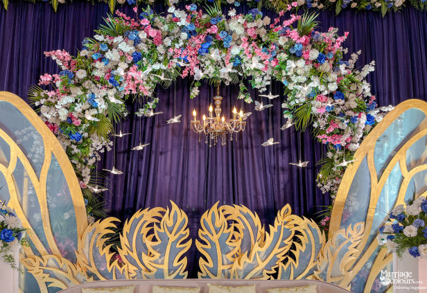 Close-up of a blue and gold stage with butterfly wings, a floral arch, and small hanging bird cutouts.