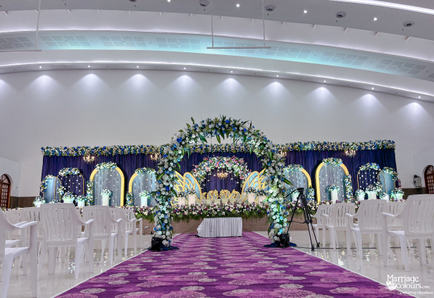Wedding stage backdrop with a large golden lotus, dense flower wall, and a plastic-covered sofa.