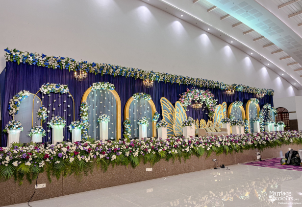 Wide-view of a lavish indoor stage with blue drapes, golden arch mirrors, and abundant white and blue flowers.