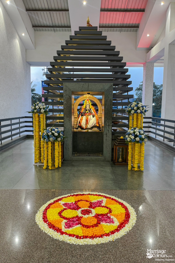 Entrance to a modern Hindu shrine with a deity idol, floral towers, and a colorful rangoli.
