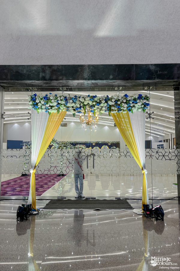 Wedding hall entrance with white and yellow drapes, a floral arch, and small chandelier.