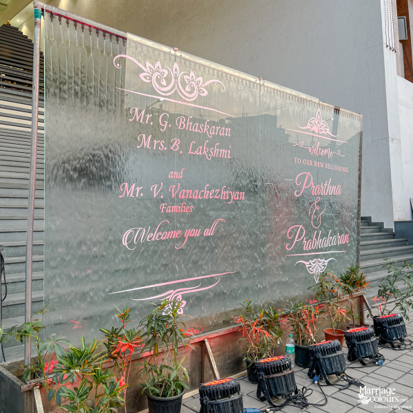 Outdoor water fountain welcome sign with pink text for Prarthna & Prabhakaran and their families.
