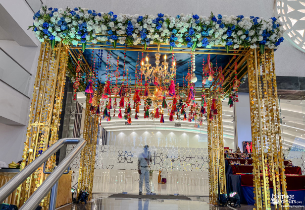 Grand entrance arch with a blue and white floral top, gold sequin strings, and colorful hanging tassels.