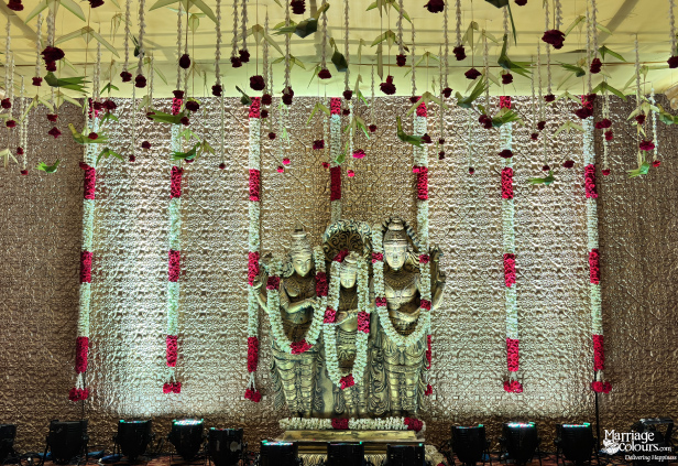 Close-up of golden Hindu deity idols on a stage, with red and white hanging flower garlands.