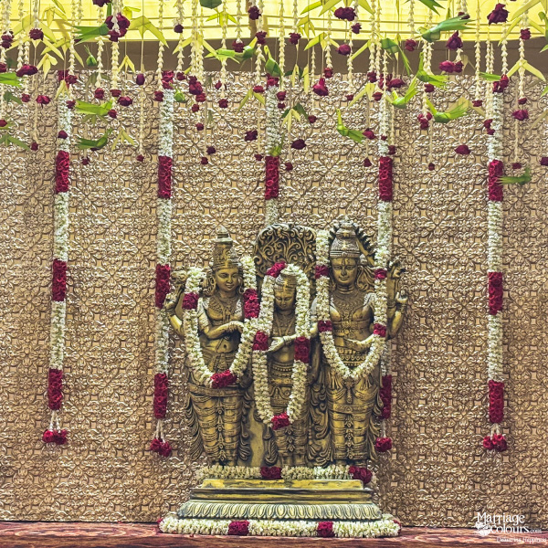 Close-up of golden Hindu deity idols on a stage, surrounded by hanging red and white flower garlands.