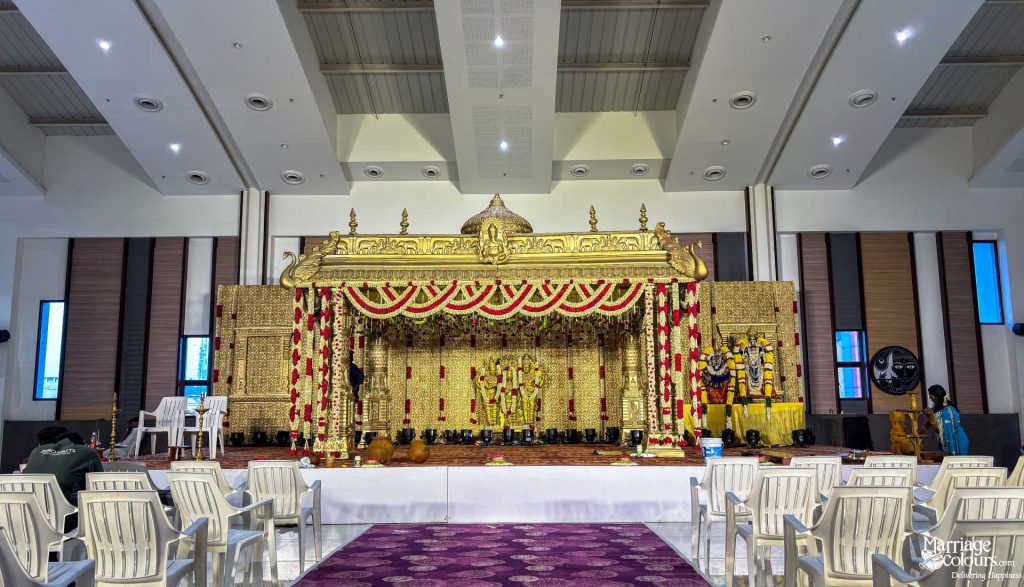 Grand golden South Indian wedding stage with traditional decor, floral garlands, and religious figures.
