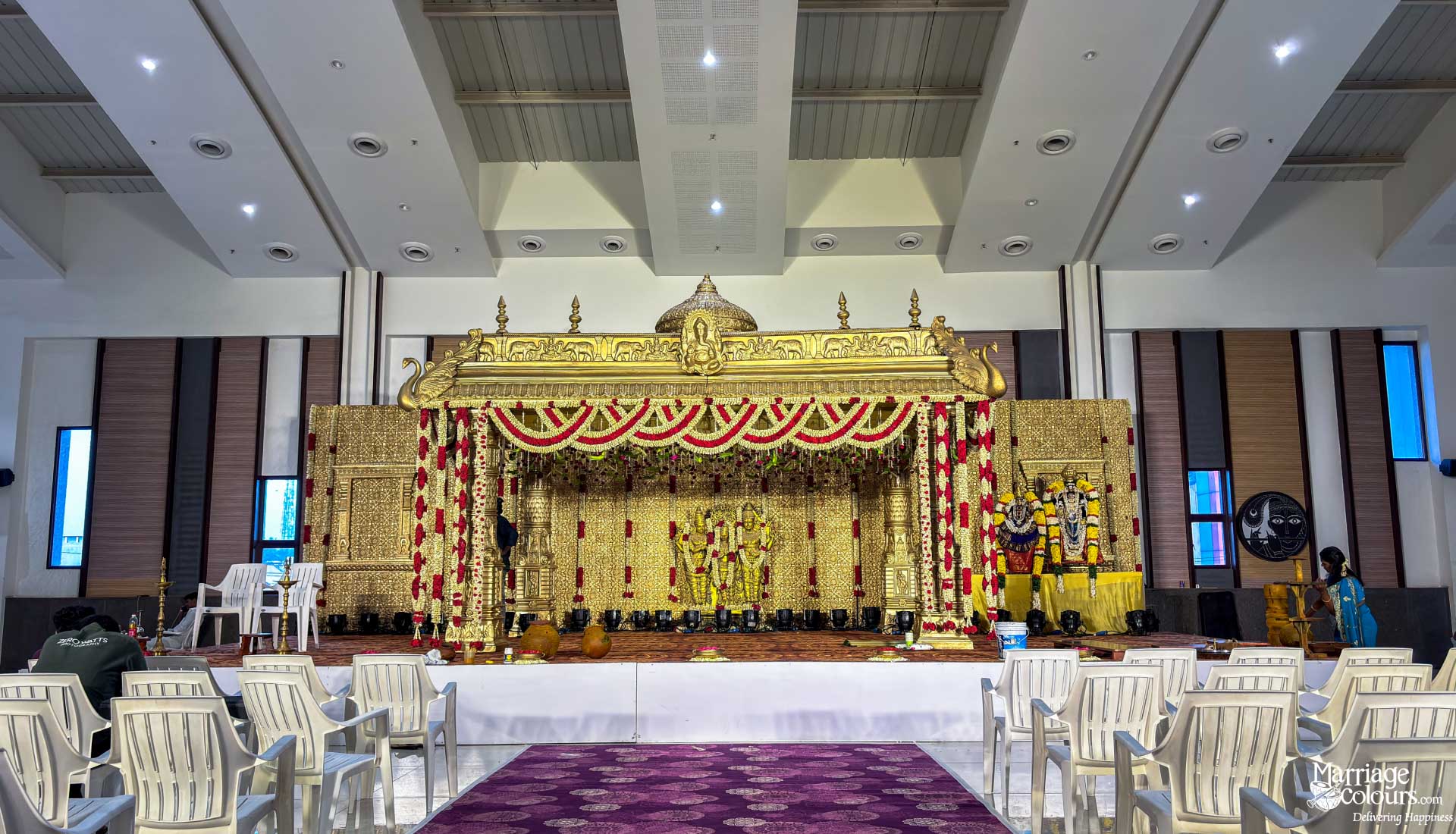 Grand golden South Indian wedding stage with traditional decor, floral garlands, and religious figures.