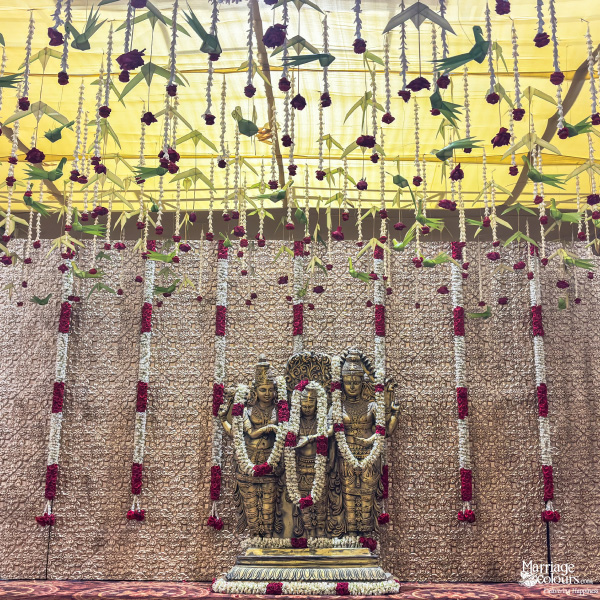 Close-up of golden deity idols on a stage, surrounded by hanging red and white flower garlands.