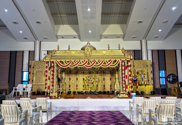 Grand golden South Indian wedding stage with traditional carved decor, floral garlands, and seating.
