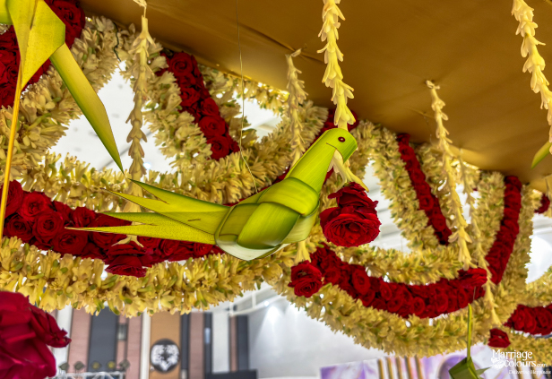 Close-up of a woven palm-leaf parrot hanging among red and white flower garlands and roses