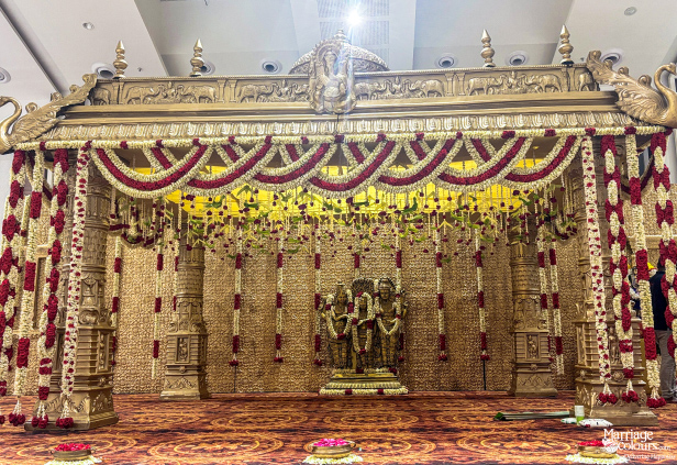 Traditional golden South Indian wedding mandap with heavy red and white flower garlands.
