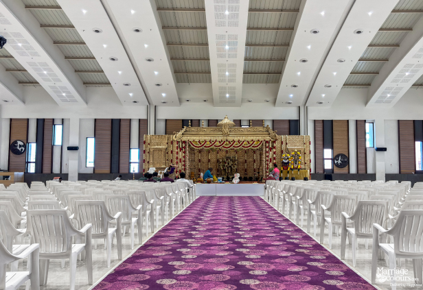 Wide view of a golden South Indian stage, purple patterned aisle, and rows of white seating.