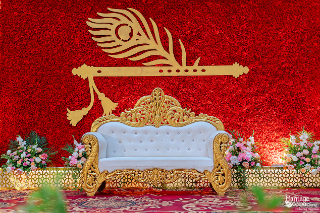 Ornate white and gold sofa on a stage with a red floral backdrop and golden flute and feather.