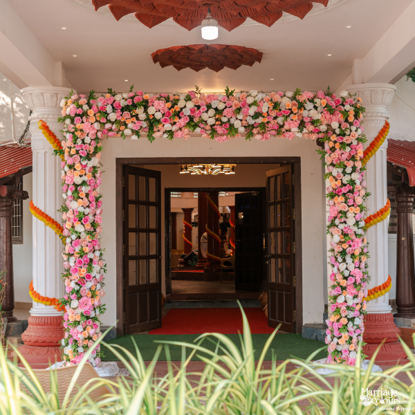 Traditional house entrance with white pillars decorated by a thick arch of pink and white flowers.