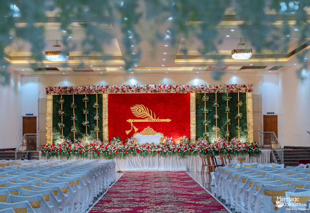 Grand hall with rows of seating and a vibrant stage featuring a red floral wall and golden motif.