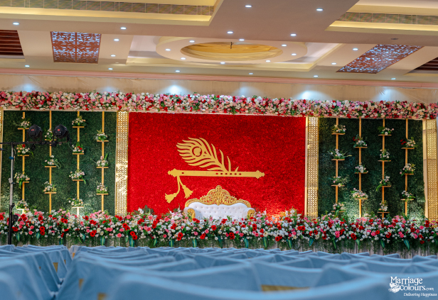 Grand wedding stage with a striking red floral wall, white and gold sofa, and green foliage panels.
