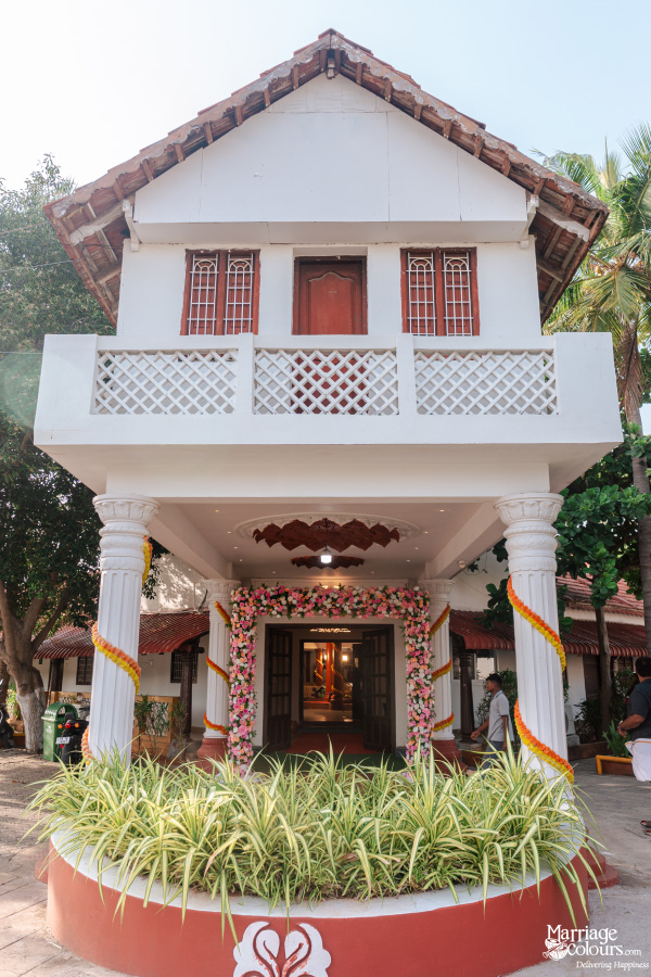 Traditional two-story white house entrance decorated with a pink and yellow floral arch for a wedding.