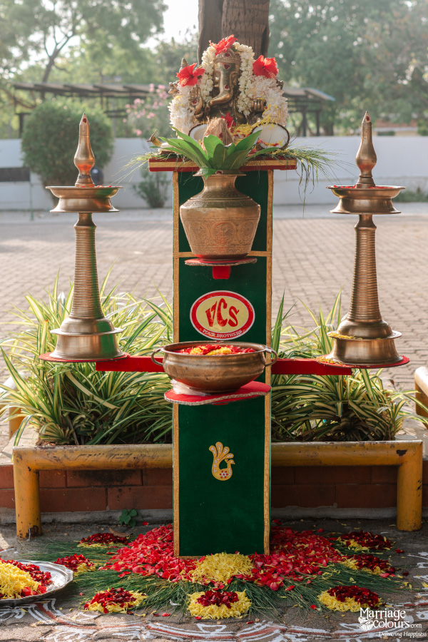 Traditional Hindu puja setup with a Ganesha idol, bronze lamps, and flower petals on a green stand.