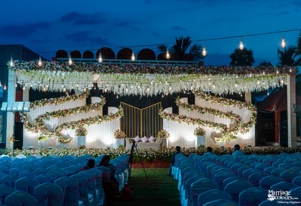 Outdoor evening wedding stage with a beige sofa, tiered floral backdrop, and hanging string lights.
