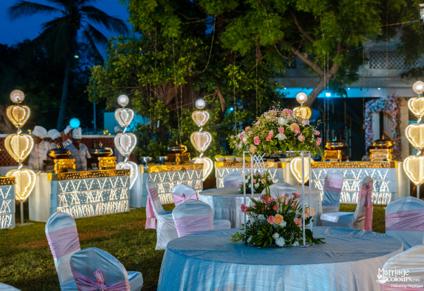 Outdoor night reception tables with white and pink decor, illuminated by heart-shaped lights and buffet.