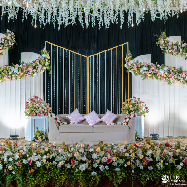 Wedding stage with a beige sofa, pink floral waves, black and gold backdrop, and hanging wisteria.