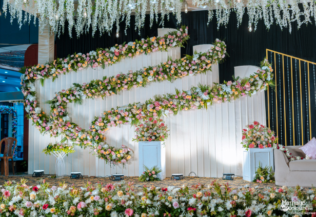 Wedding stage background with white drapes, sweeping floral garlands, and hanging wisteria.