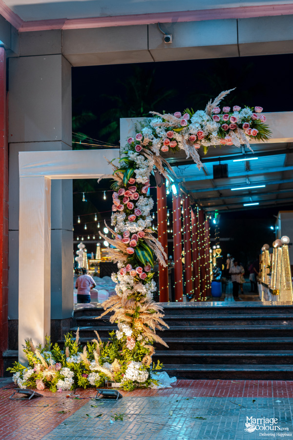 Modern white arch decorated with pink roses and dried pampas grass at an evening outdoor event.