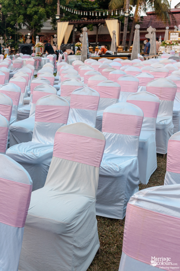 Rows of white chair covers with pink sashes set up on a lawn for an outdoor event.
