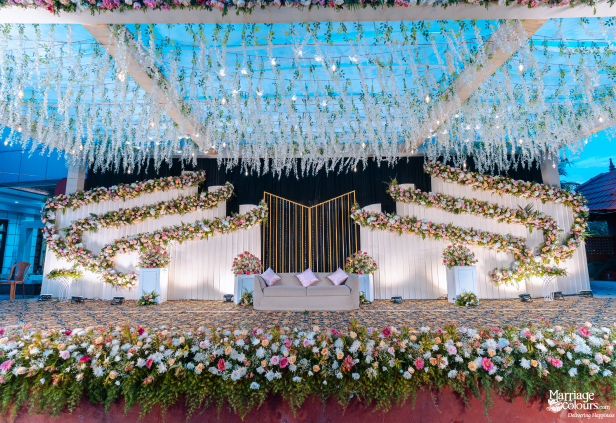 Outdoor wedding stage with a beige sofa, cascading white wisteria, and a pink and white floral motif.