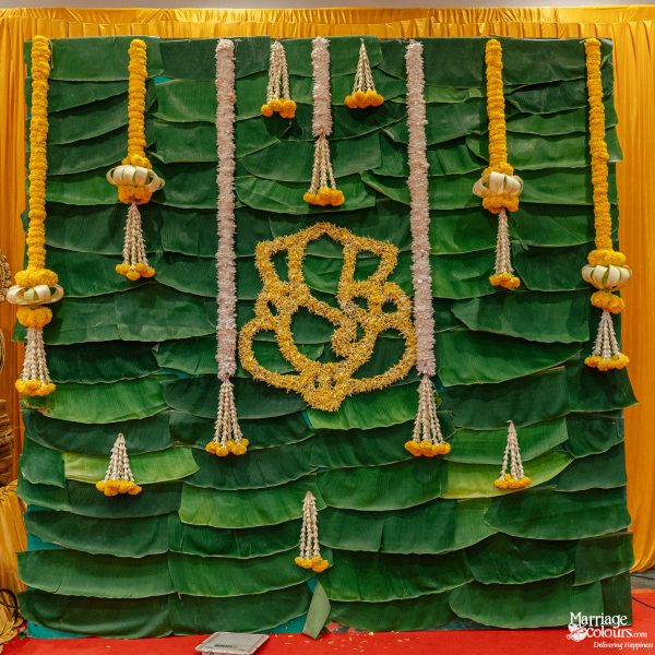 Traditional backdrop made of banana leaves, adorned with yellow and white flower garlands and a Ganesha motif.