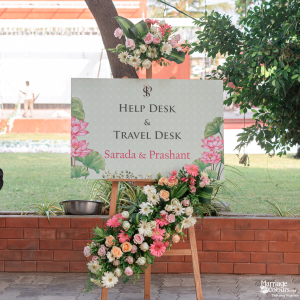 Wedding help desk sign for Sarada and Prashant, decorated with pink, white, and peach floral arrangements.