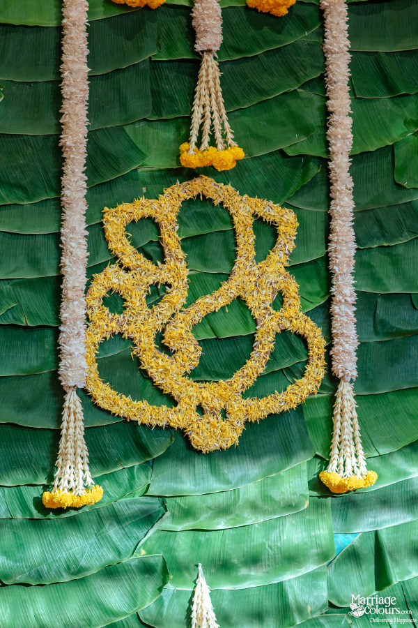 Close-up of a traditional backdrop of banana leaves decorated with a Ganesha motif made of yellow flowers.