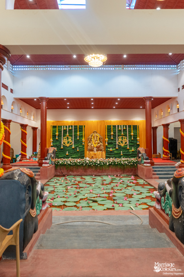 Grand hall with elephant statues framing a lotus pond and a Hindu-themed stage with a Ganesha idol.
