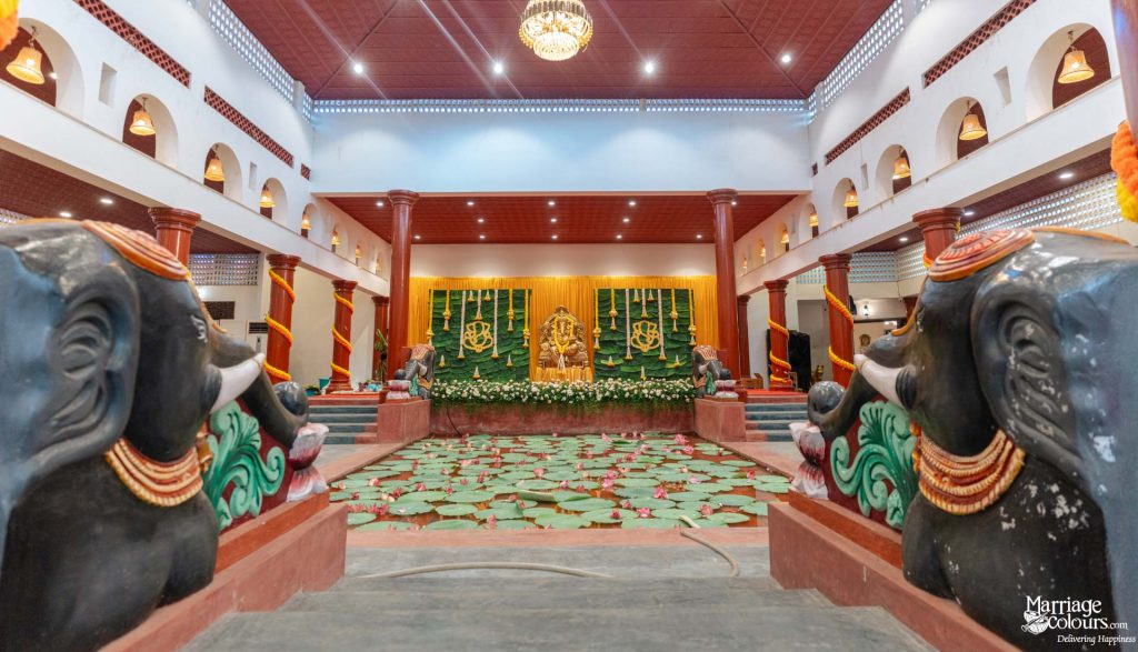 Grand traditional hall with elephant statues framing a lotus pond and a Hindu-themed stage.