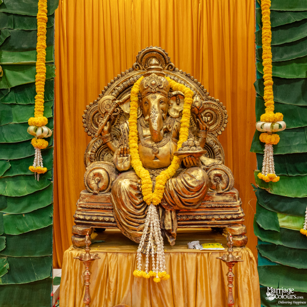 Close-up of a golden Ganesha idol on a throne, garlanded with marigolds, against a yellow and green backdrop.