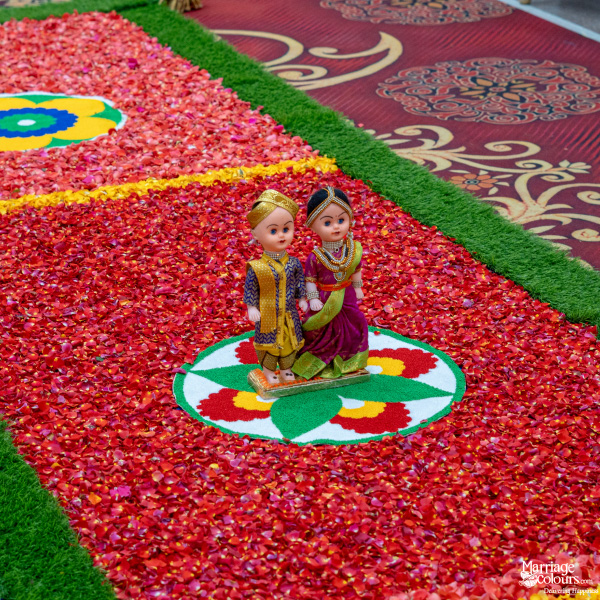 Wedding path decorated with red rose petals, artificial green turf, and traditional bride and groom dolls.