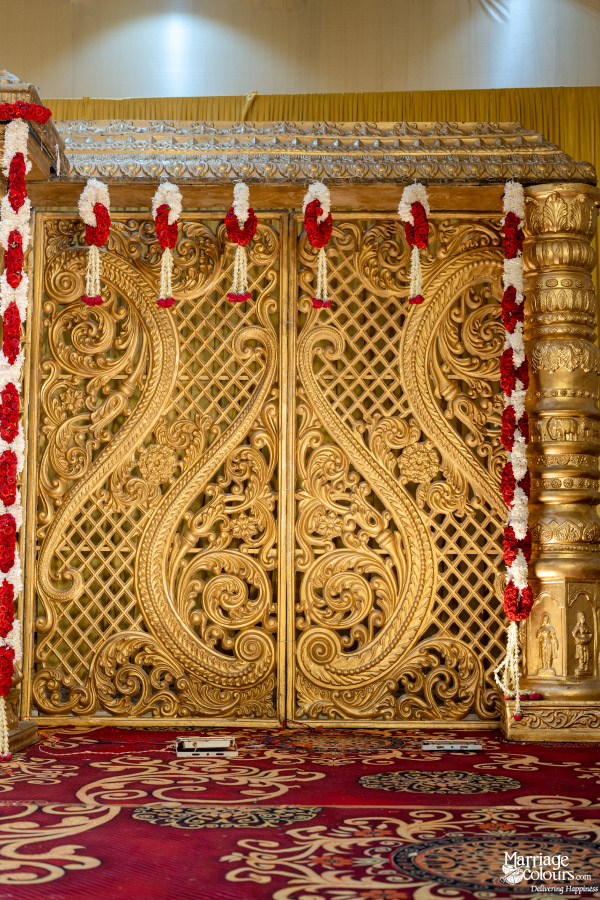 Close-up of traditional wedding stage backdrop with ornate golden carved panels and red and white flower garlands.