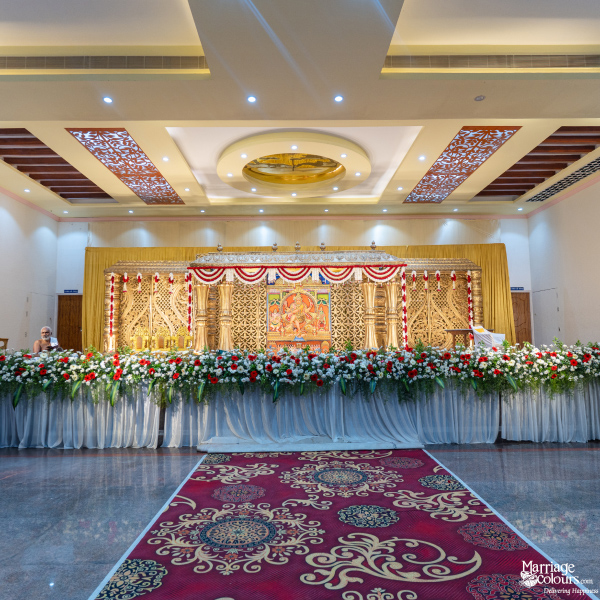 Grand wedding hall with a traditional gold-carved stage, red carpet, and a large red and white floral border.